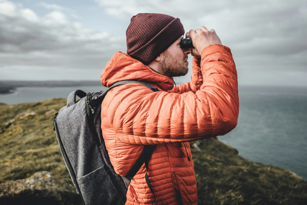 Man looking through his binoculars to the sky over the cliffs