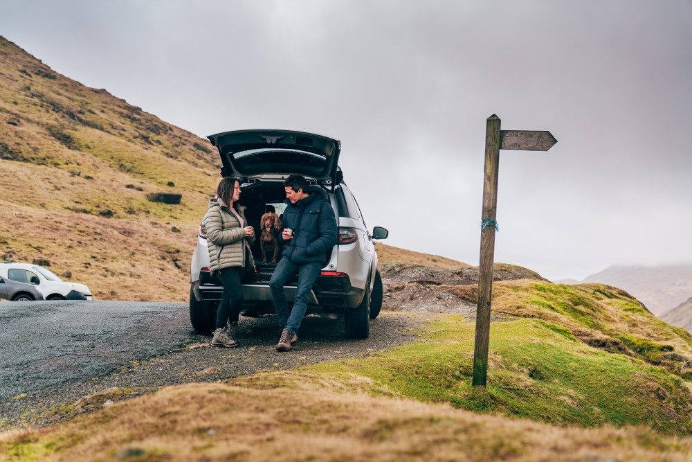 Man and woman stood at the boot of their Land Rover Discovery with the dog in the boot