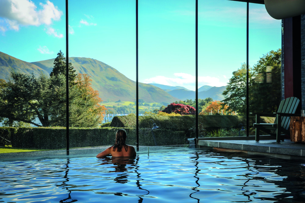 Woman looking out of the picture window over the fells from the pool at Another Place, The Lake