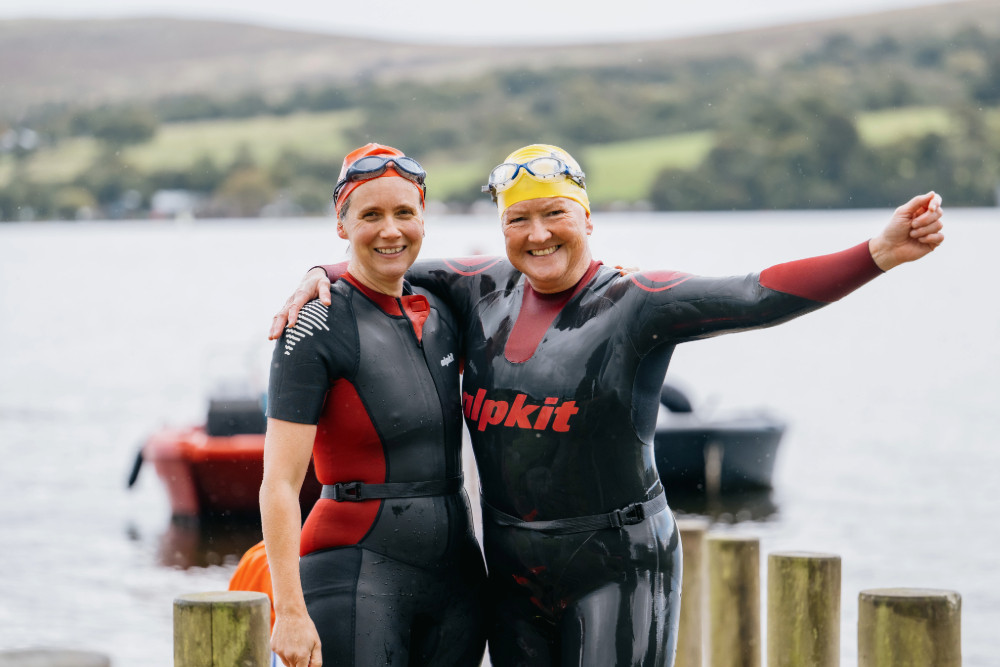 Two people in wetsuits and swimming caps on the jetty after going in Ullswater late